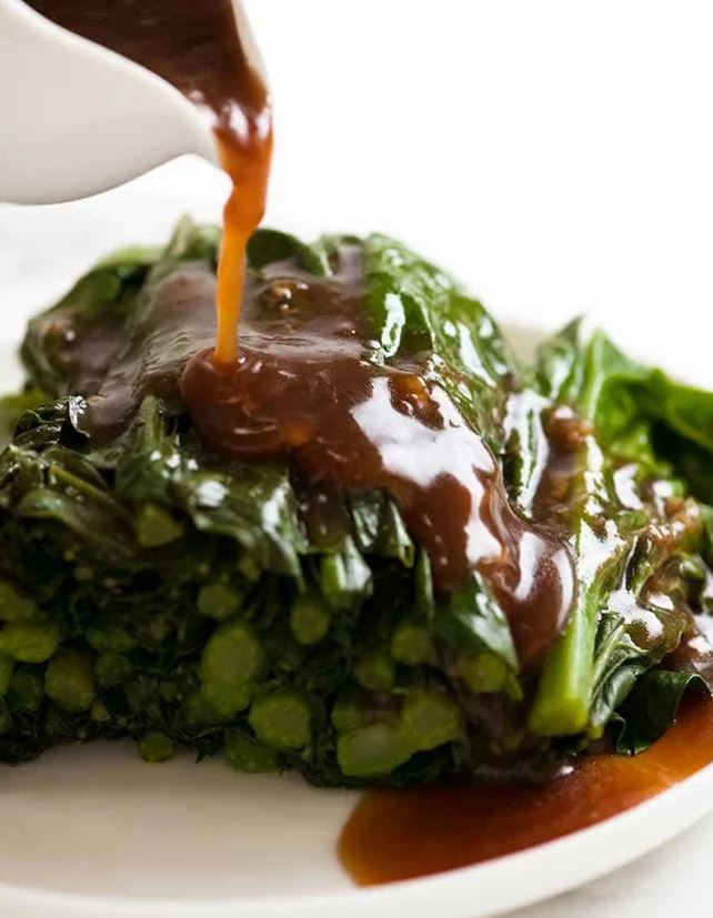 A plate of chinese broccoli with oyster sauce being poured over the top.