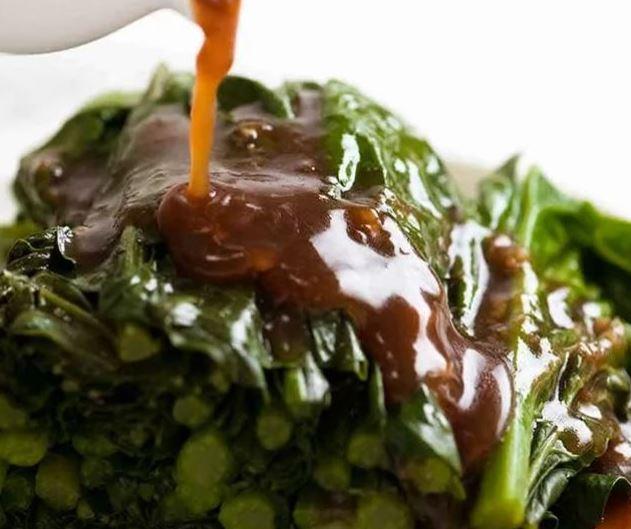 A plate of chinese broccoli with oyster sauce being poured over the top.
